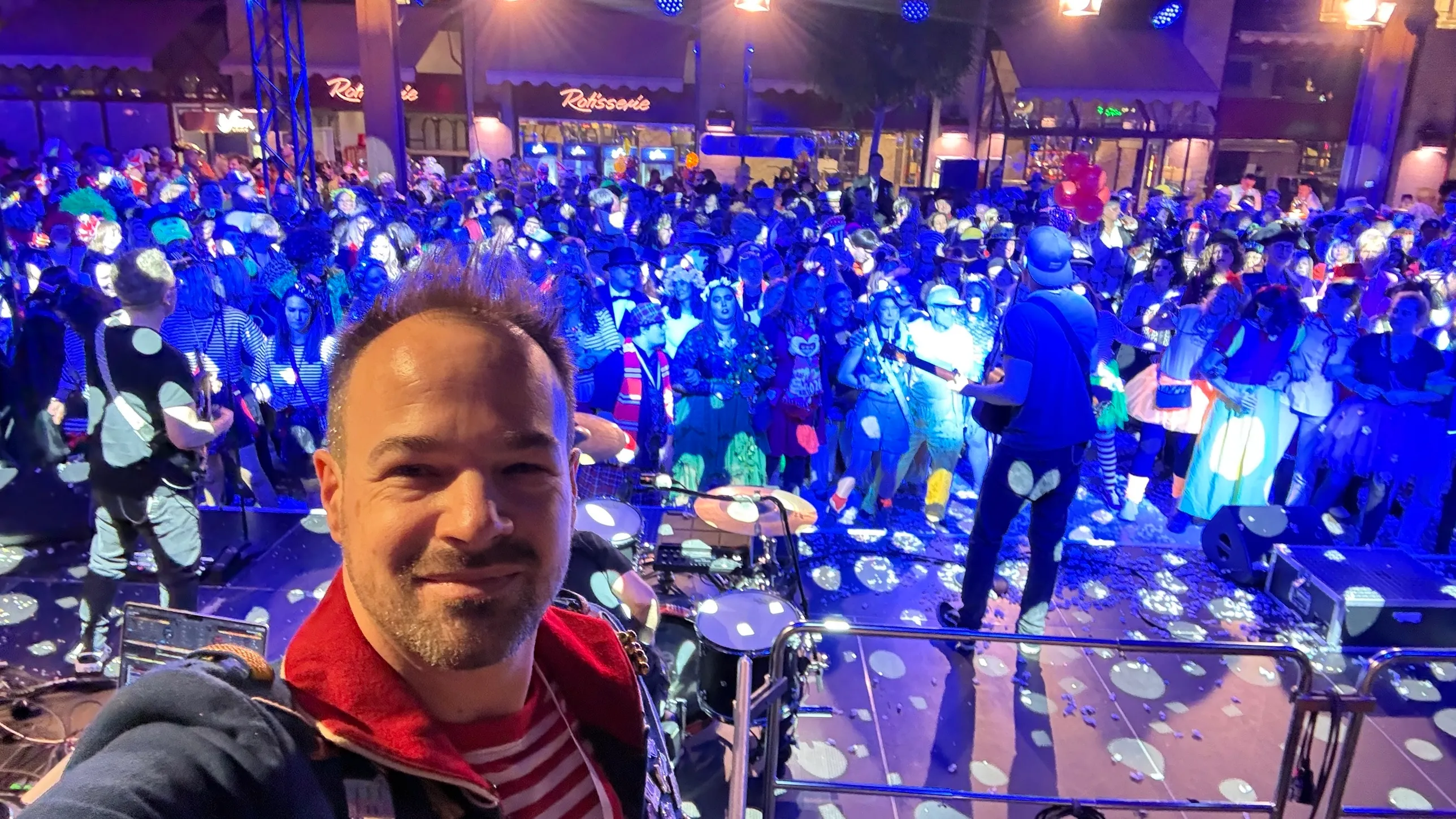Selfie von René Braun auf der Bühne, dahinter Band und volle Passage im blauen Licht
