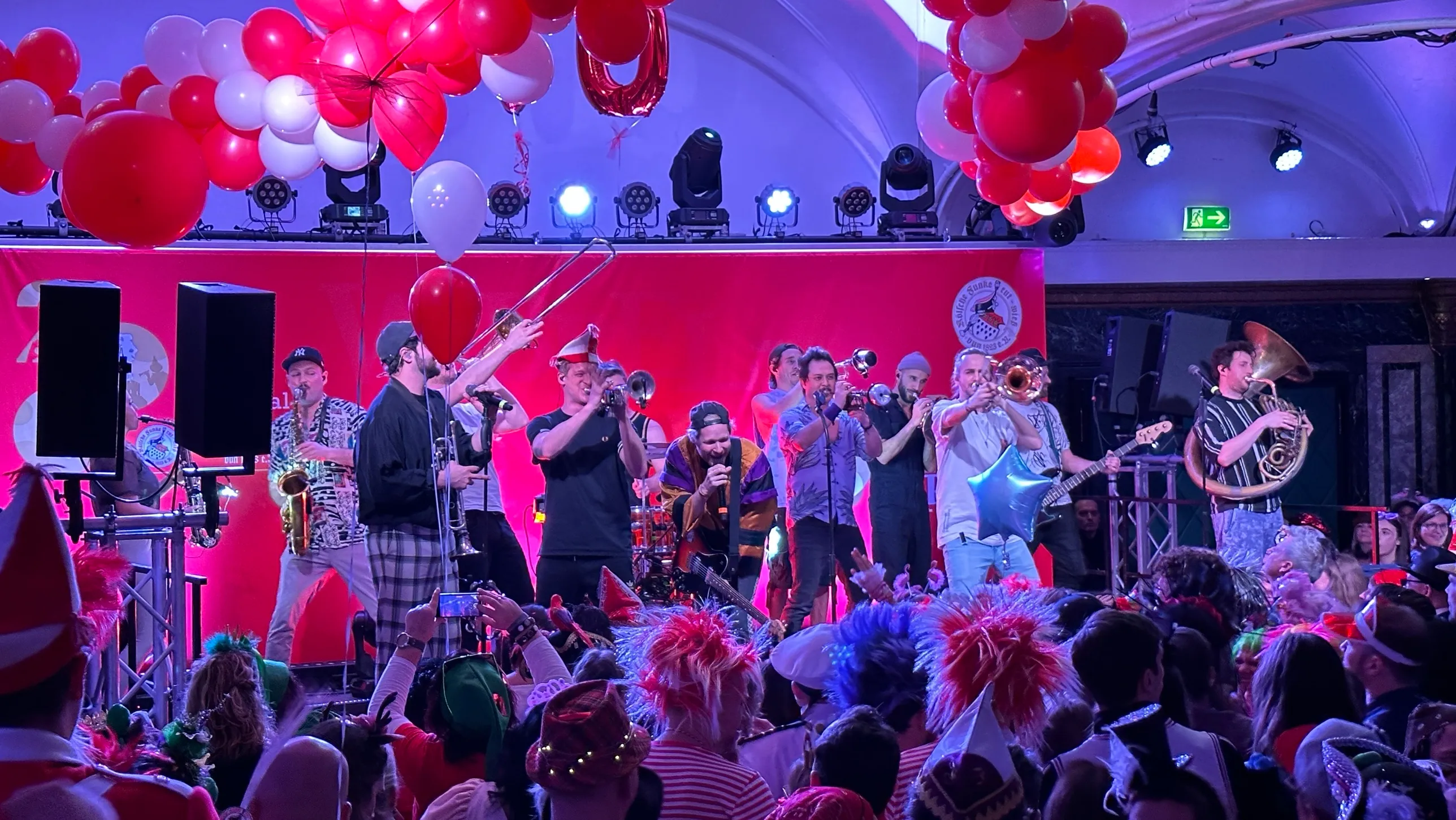 Bläserband auf der Bühne der Wibbeldance-Party, rote und weiße Luftballons über dem Saal